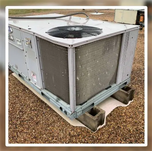 A large air conditioner unit sitting on top of gravel.