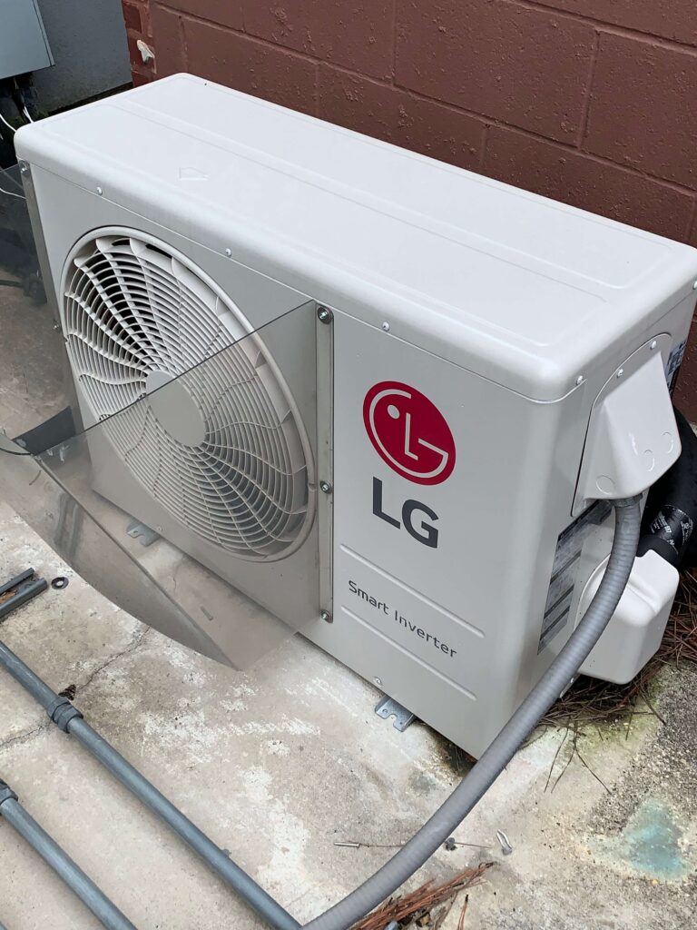 A white air conditioner sitting on top of the ground.